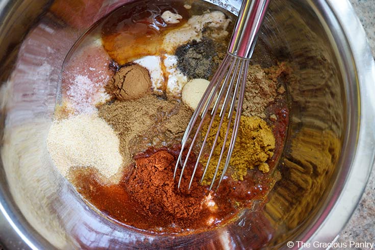 A mixing bowl filled with yogurt and various spices. A whisk rests in the bowl.