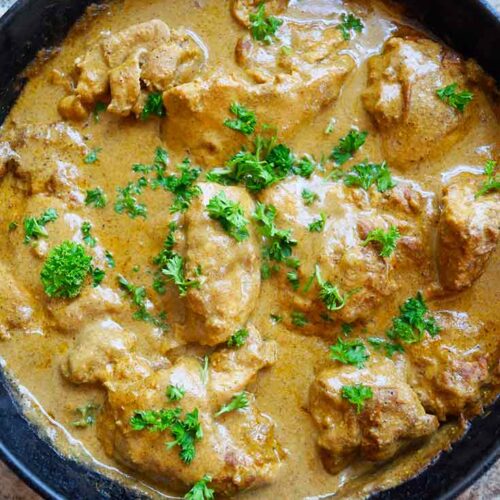 An overhead view of a cast iron skillet show a pan full of Yogurt Chicken, baked and garnished with fresh, chopped parsley.