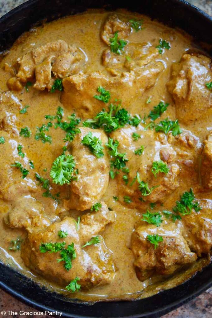 A close up of Yogurt Chicken in a cast iron skillet garnished with fresh parsley.