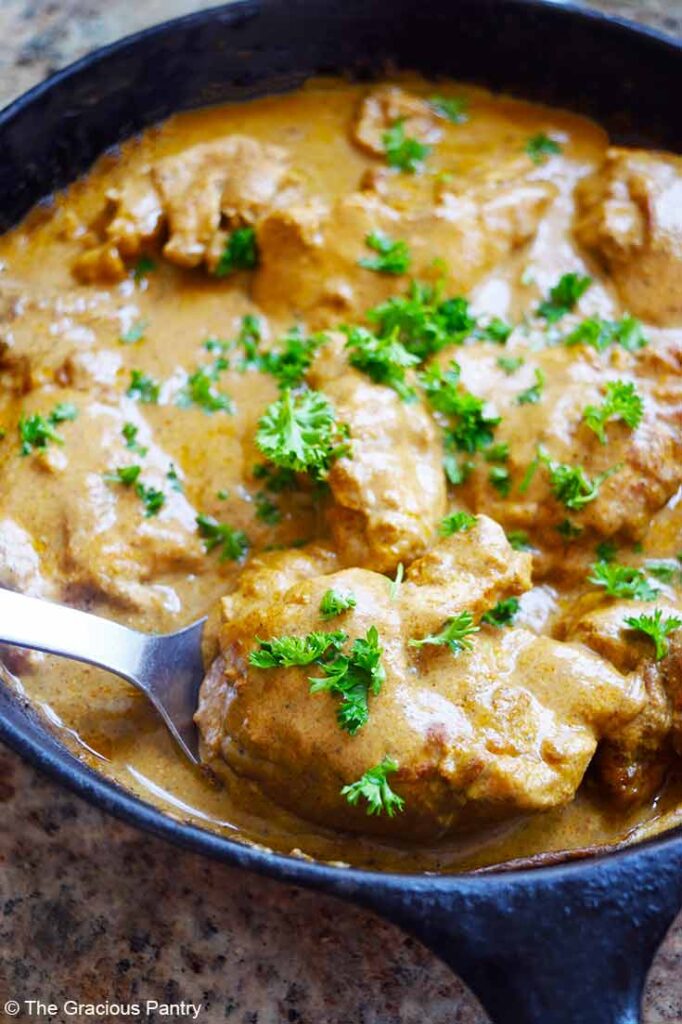 A spoon picks up a piece of yogurt chicken from a cast iron skillet.