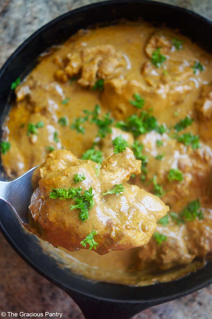 A close up of a serving spoon holding a piece of yogurt chicken over a skillet.