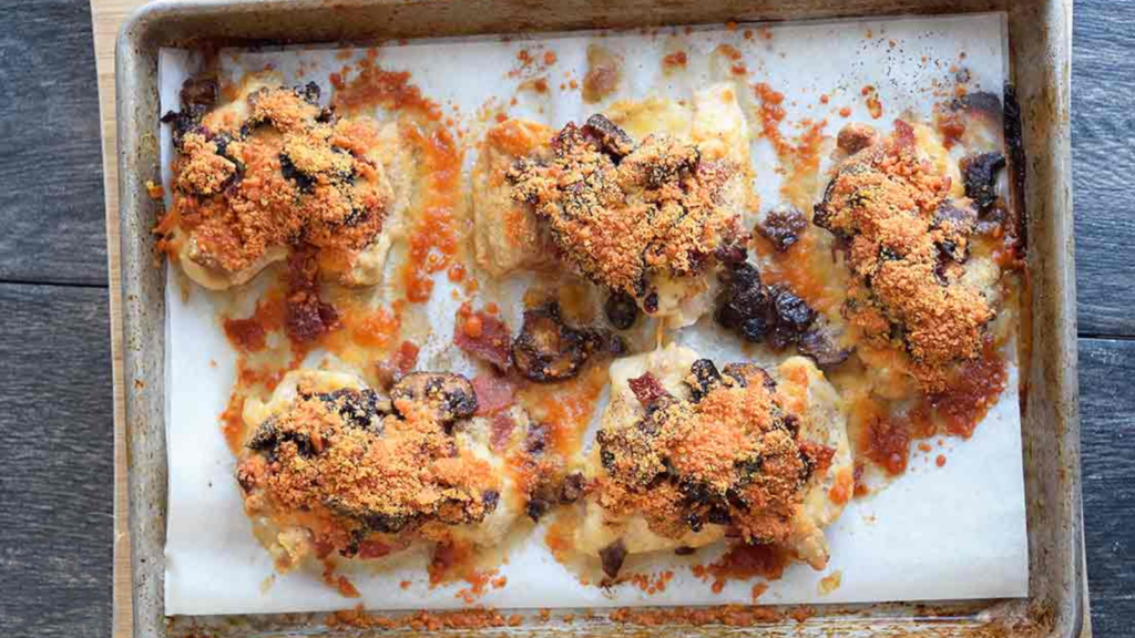 An overhead view of bacon stuffed chicken thighs on a parchment-lined baking pan.