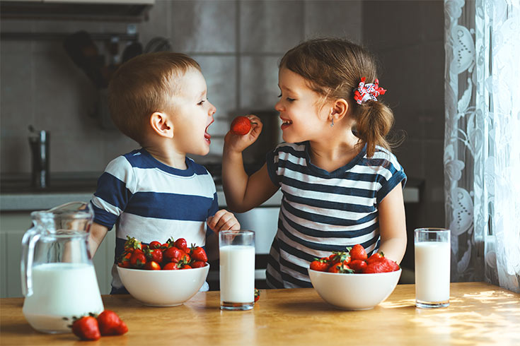 Two young kids eating strawberries.