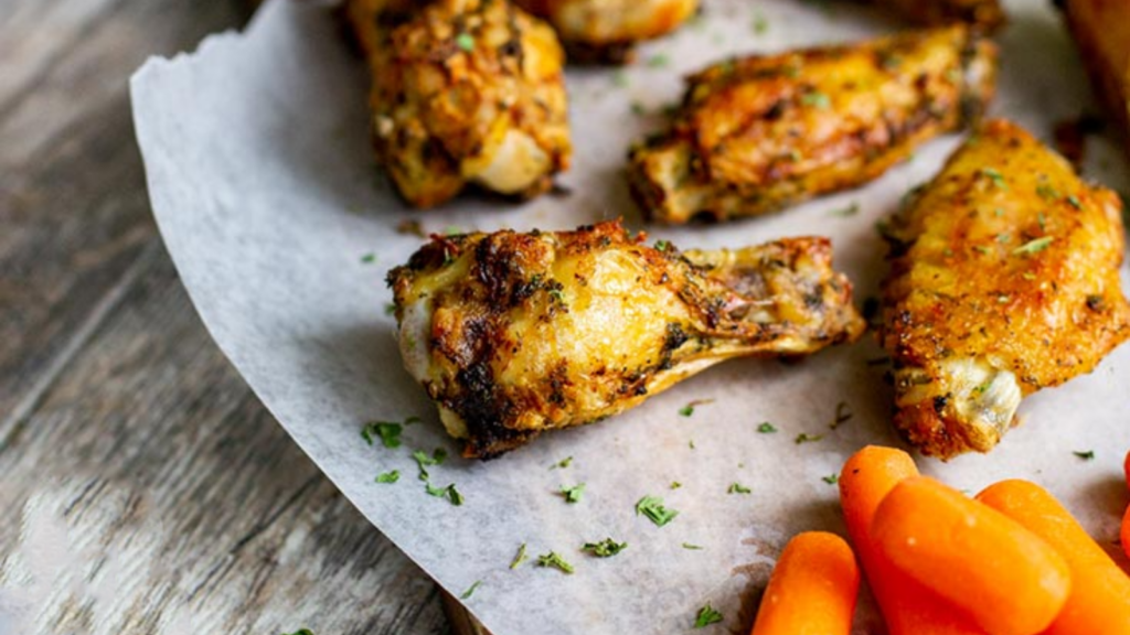 A few golden brown chicken wings laying on a piece of parchment paper.