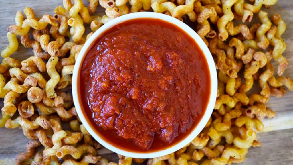 An overhead view of air fryer pasta chips on a cutting board with a white bowl of marinara in the middle.