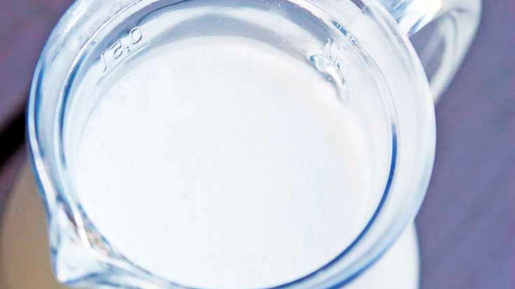 An up close view of a glass pitcher filled with almond milk.