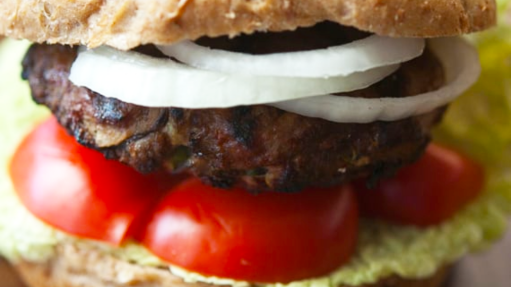 A closeup of an Asian Mushroom Burger with tomatoes and onion slices.