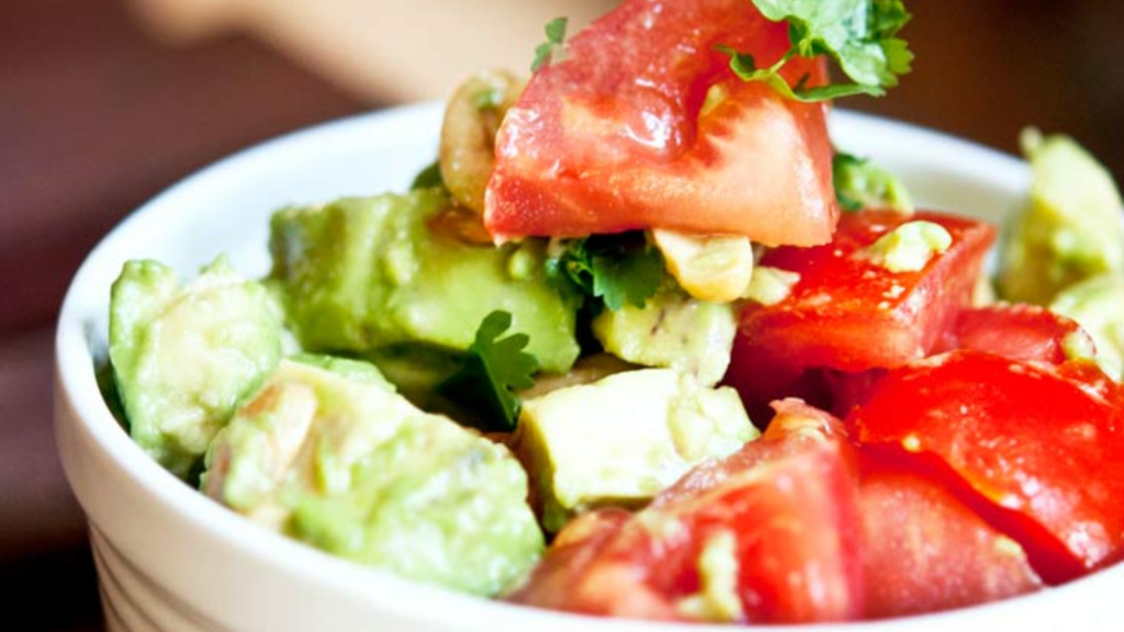 A closeup of a white bowl filled with avocado cashew salad.