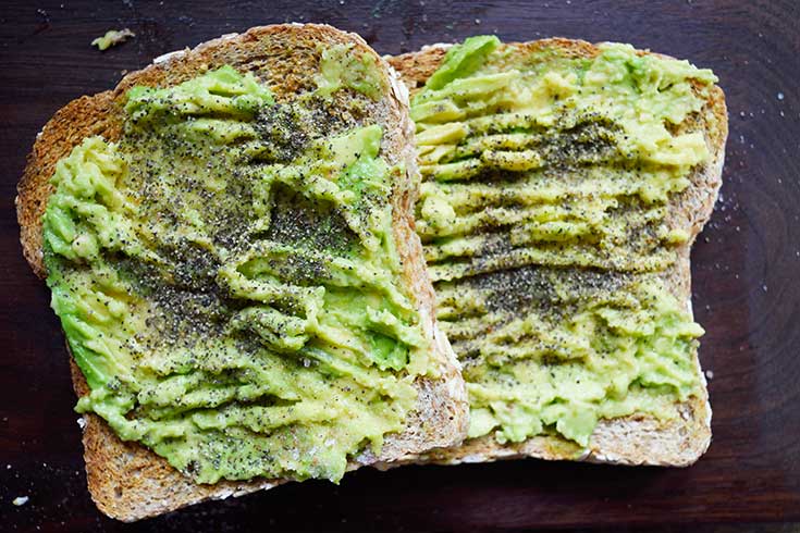 Two slices of avocado toast on a dark wood background.