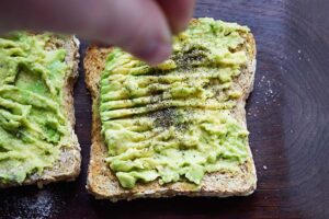 Sprinkling ground pepper over avocado toast.