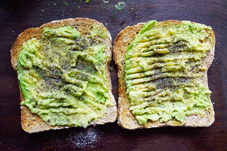 Two slices of finished avocado toast laying on a dark wood cutting board.