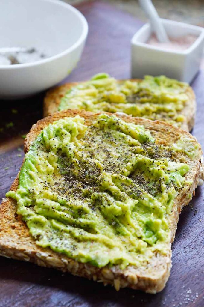 An up close view of a piece of avocado toast with ground black pepper sprinkled over it.