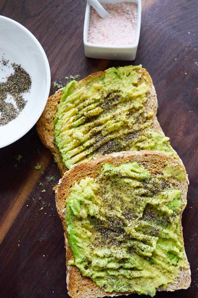 An overhead view of two pieces of avocado toast laying on a wood cutting board.