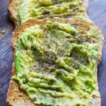 A front view of two pieces of avocado toast on a dark wood cutting board.
