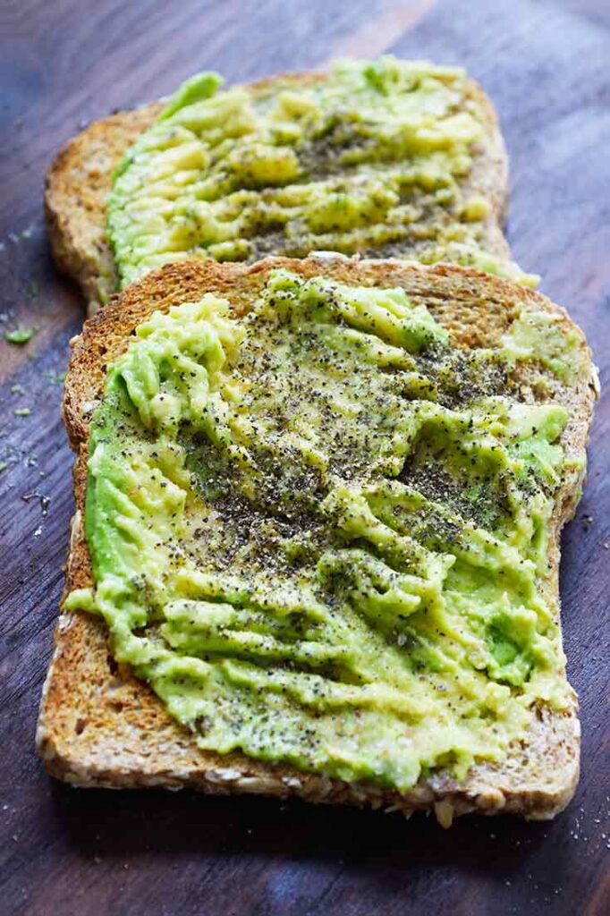 A front view of two pieces of avocado toast on a dark wood cutting board.