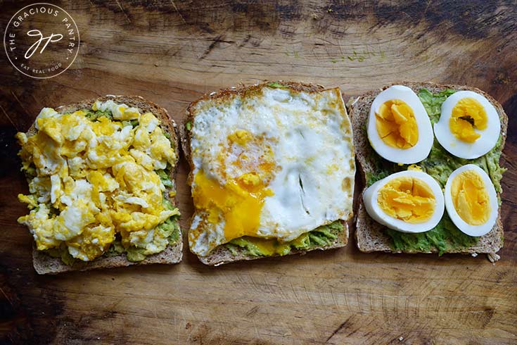 A lineup of three slices of bread. One with scrambled eggs, one with a fried egg and one with hard-boiled egg slices.