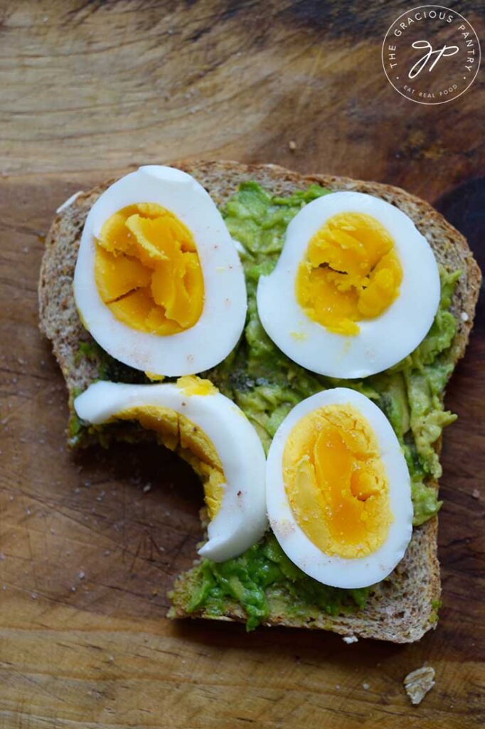 A single slice of Avocado Toast With slices of hard-boiled egg on top. A bit has been taken from the toast.