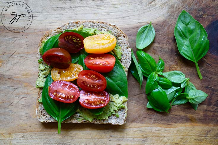 Tomatoes placed on top of the basil leaves on the avocado toast.