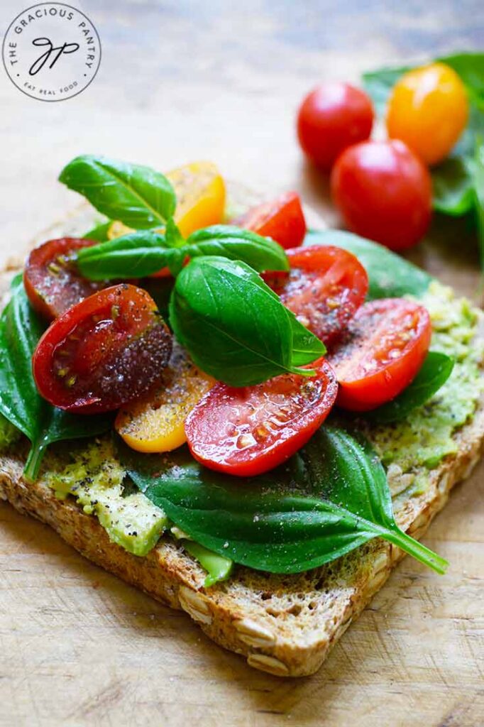 A side view of a slice of Avocado Toast With Tomato laying on a wooden surface.