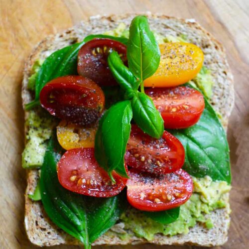 An overhead view of a slice of Avocado Toast With Tomato laying on a wood surface.