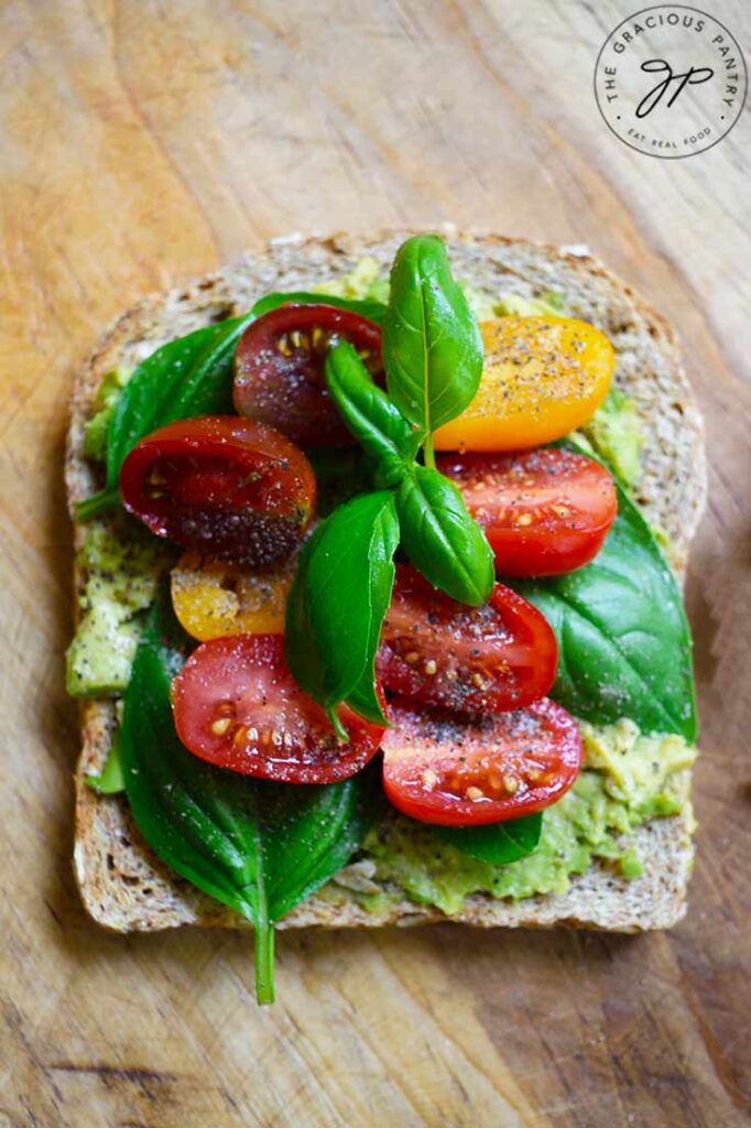 An overhead view of a slice of Avocado Toast With Tomato laying on a wood surface.
