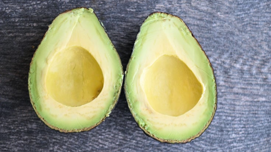 Two avocado halves sit side by side on a gray surface.