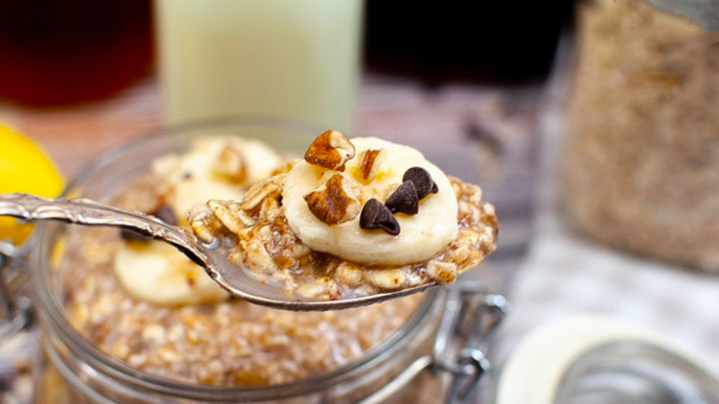 A spoon lifts some banana bread oatmeal from a jar that is full of it.
