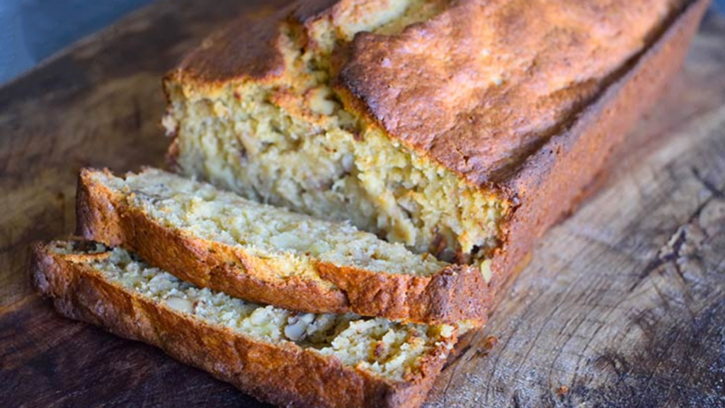 A loaf of oat flour banana bread lays partially sliced on a cutting board.