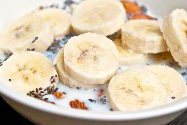 A closeup of a white bowl filled with banana muesli. Fresh banana slices cover the surface.