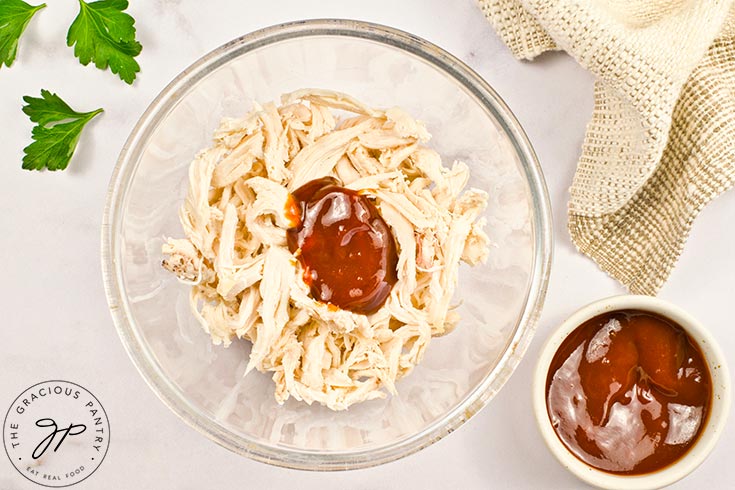 Barbecue sauce added to shredded chicken in a glass bowl.