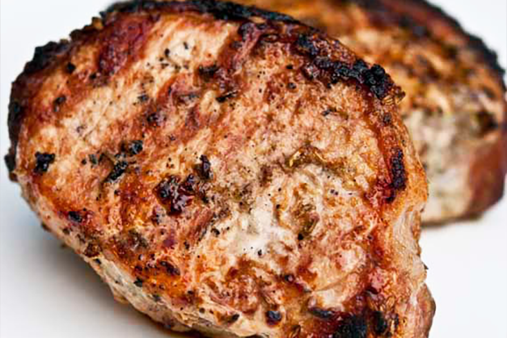 a closeup of two bbq fennel pork chops on a white background.