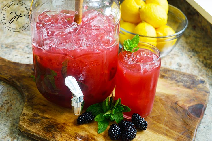 The finished Blackberry Lemonade in a large jug of ice and served in a glass.