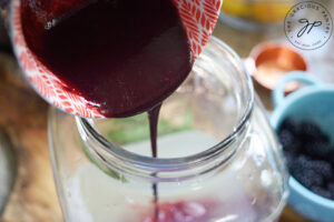 Adding the blackberry juice to a large beverage jug.