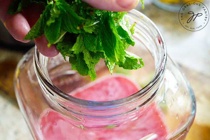 Adding fresh mint leave to a large beverage jug of blackberry lemonade.