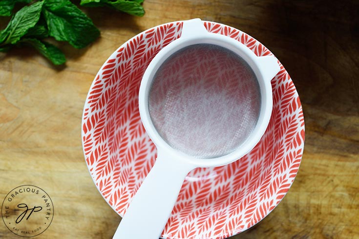 A fine-meshed strainer sits over a bowl for straining the blackberries after blending.