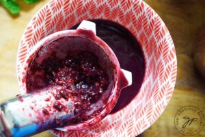 Straining blended blackberries through a strainer into a small bowl.