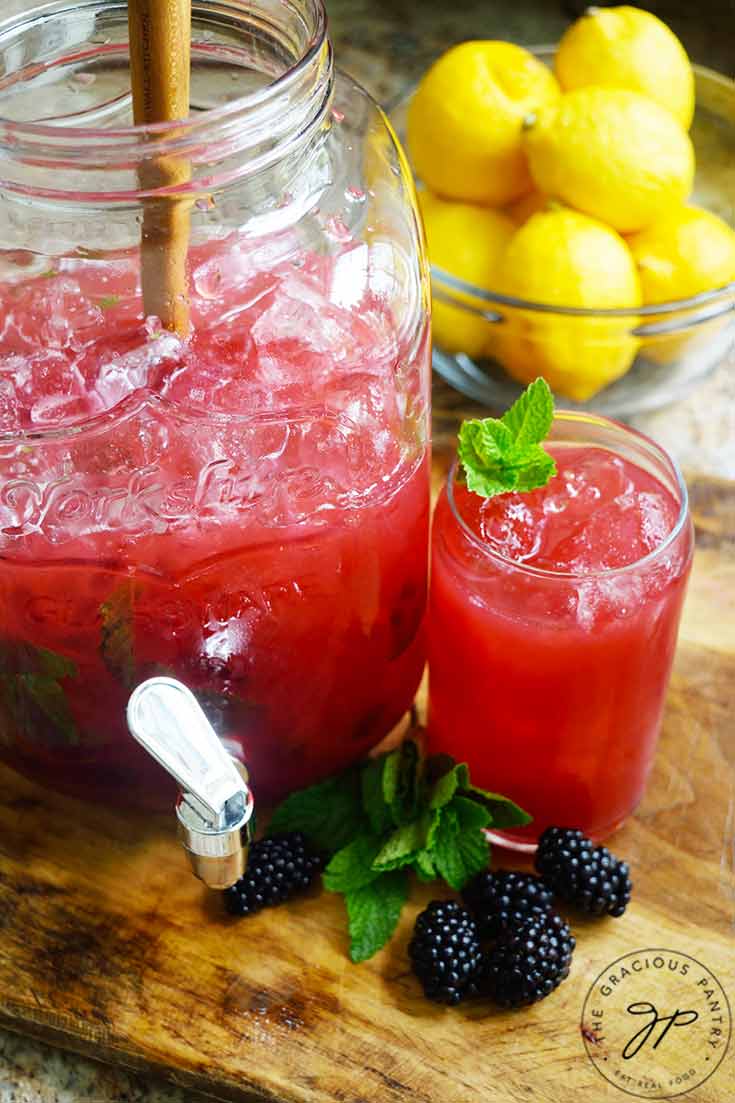 A just and glass sit on a wood cutting board, both holding Blackberry Lemonade.
