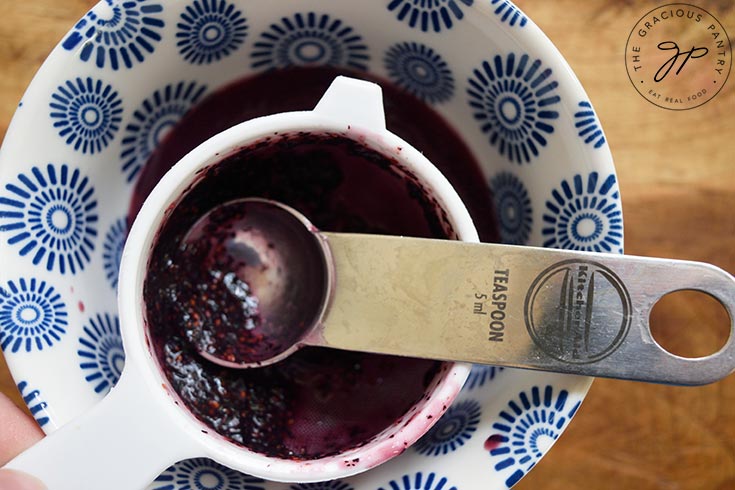 Pressing blueberry pulp through a mesh strainer.