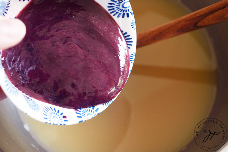 Pouring blueberry puree into a bowl of lemon juice, water and sweetener.