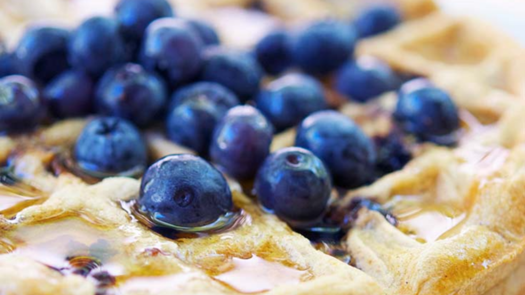 A closeup of a blueberry waffle with fresh blueberries on top.