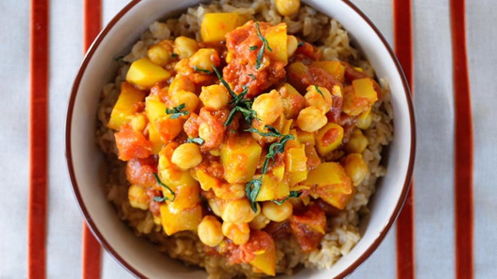 An overhead view of a bowl of Bombay potatoes in a bowl on a striped tablecloth.