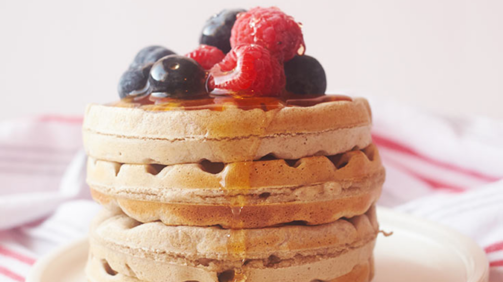 A stack of buckwheat waffles with fresh berries and syrup on top.