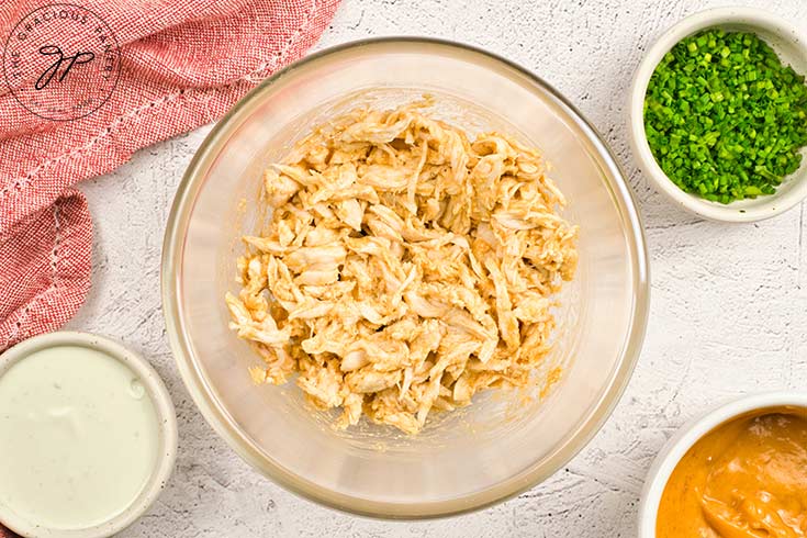 Shredded chicken mixed with the buffalo sauce in a mixing bowl.