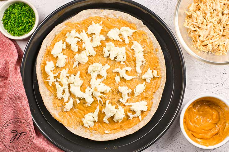 Cheese spread over the pizza crust and sauce which lays on a pizza pan.