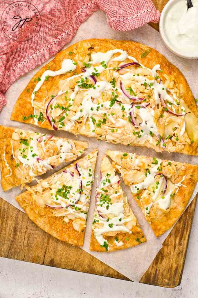 A Buffalo Chicken Pizza half cut and laying on a wooden cutting board.