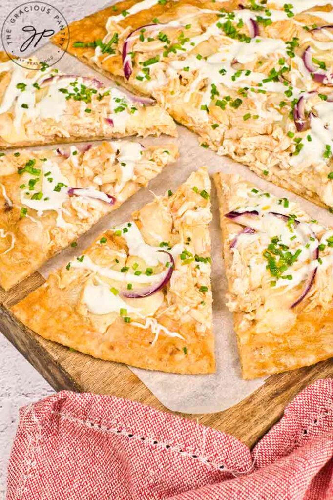 A half cut Buffalo Chicken Pizza from the side, lays on a cutting board.