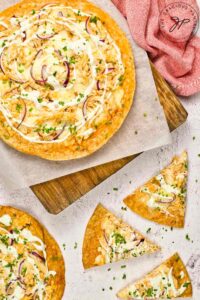 Two whole Buffalo Chicken Pizzas and a few slices lay on a white surface and a cutting board.