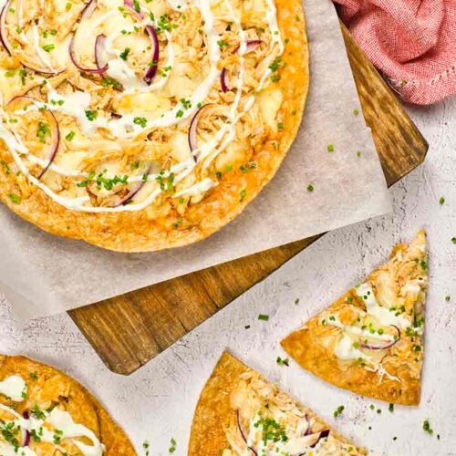 Two whole Buffalo Chicken Pizzas and a few slices lay on a white surface and a cutting board.