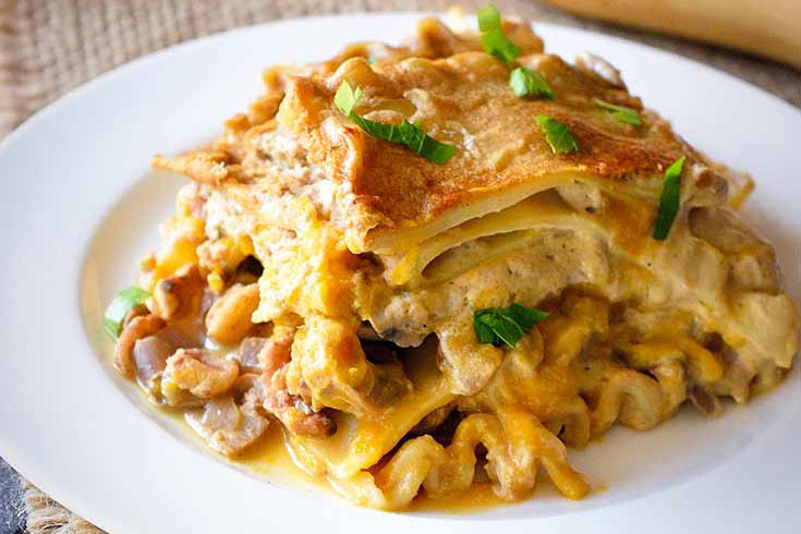 A serving of butternut lasagna on a white plate garnished with chopped greens.