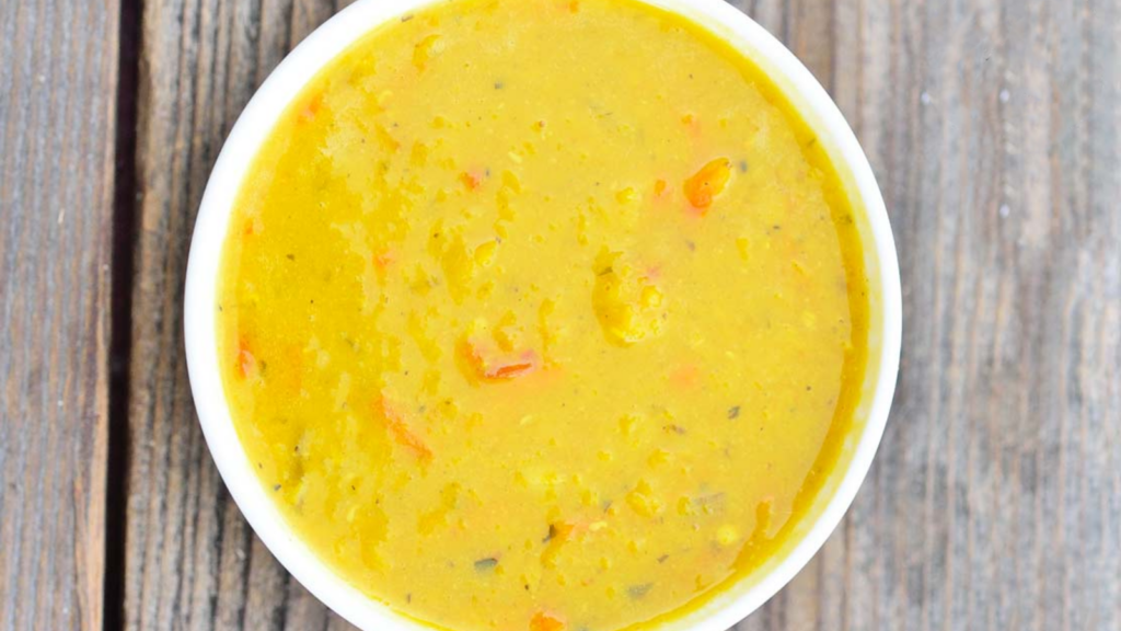 An overhead view of a white bowl filled with Carrot Ginger Lentil Soup.